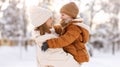 Happy family enjoying snowy weather outdoor, mom with little son hugging during walk in winter park Royalty Free Stock Photo