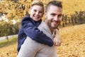 Happy family father and child boy in the autumn leaf fall in park holding his child on his back Royalty Free Stock Photo