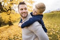 Happy family father and child boy in the autumn leaf fall in park holding his child on his back Royalty Free Stock Photo