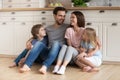 Happy family of four sitting on wooden floor at kitchen. Royalty Free Stock Photo