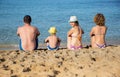 happy family of four people sit with their backs on sandy beach against backdrop of blue sea Royalty Free Stock Photo