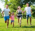 Happy family of four running on grass at summer park