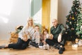 Happy family of four sits near Christmas tree with gift boxes and looking to camera Royalty Free Stock Photo