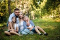 Happy family of four sitting on a grass in summer park outdoors and smiling Royalty Free Stock Photo