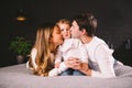 Happy family is having fun in bedroom. Enjoying being together. Parents are tickling their little son while lying in bed Royalty Free Stock Photo