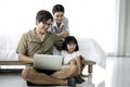 Happy family having fun in the bedroom. Father using laptop computer for working at home or shopping online, mother lying on bed