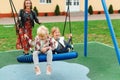 Happy family having fun together on playground. Happy childhood. Family vacation. Joyful little girls enjoying at modern swing. Royalty Free Stock Photo