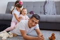 Happy family having fun together while playing on floor near sofa in light living room, father looking at camera with positive Royalty Free Stock Photo