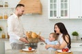 Happy family in home kitchen married couple with small child - baby takes bread Royalty Free Stock Photo