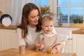 Happy family at home. Mother feeding her baby boy from spoon in kitchen. Little toddler child with messy funny face eats Royalty Free Stock Photo