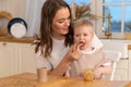 Happy family at home. Mother feeding her baby boy from spoon in kitchen. Little toddler child with messy funny face eats Royalty Free Stock Photo