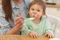 Happy family at home. Mother feeding her baby girl from spoon in kitchen. Little toddler child with messy funny face Royalty Free Stock Photo