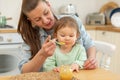 Happy family at home. Mother feeding her baby girl from spoon in kitchen. Little toddler child with messy funny face Royalty Free Stock Photo