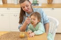 Happy family at home. Mother feeding her baby girl from spoon in kitchen. Little toddler child with messy funny face Royalty Free Stock Photo