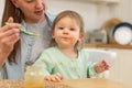 Happy family at home. Mother feeding her baby girl from spoon in kitchen. Little toddler child with messy funny face Royalty Free Stock Photo