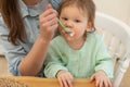 Happy family at home. Mother feeding her baby girl from spoon in kitchen. Little toddler child with messy funny face Royalty Free Stock Photo