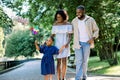 Happy family, joyful time together outdoors. Dark skinned little girl in blue dress, blowing colorful windmill toy Royalty Free Stock Photo