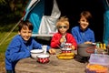 Happy family, kids, boy brothers and a dog, having breakfast in front of pitched tent in the forest, while wild camping in Norway Royalty Free Stock Photo