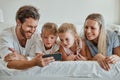 Happy family with kids, phone and lying on bed in home, mother, father and girl children watching video together. Love Royalty Free Stock Photo