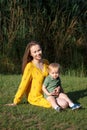 Happy family leisure outdoors. Portrait of smiling young woman holding little toddler son in arms. They are sitting on the green Royalty Free Stock Photo