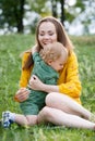 Happy family leisure outdoors. Portrait of smiling young woman holding little toddler son in arms. They are sitting on the green Royalty Free Stock Photo