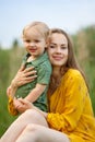 Happy family leisure outdoors. Portrait of smiling young woman holding little toddler son in arms. They are sitting on the green Royalty Free Stock Photo