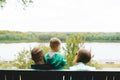 Happy family with little child sitting on a bench in spring park, looking the lake. Back view Royalty Free Stock Photo