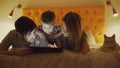 Happy family with little son and funny cat lying in bed at home and using tablet computer for playing game before Royalty Free Stock Photo