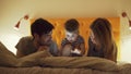 Happy family with little son learning to play tablet computer lying in bed at home in evening Royalty Free Stock Photo