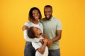 Happy family. Loving african american parents with daughter embracing and smiling at camera over yellow background Royalty Free Stock Photo