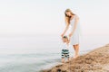 Happy family, mom and baby are walking along the evening beach during sunset