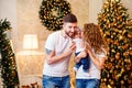 Happy family. Mom and dad hugging and kissing little baby girl while standing near Christmas tree Royalty Free Stock Photo