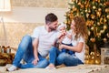 Happy family. Mom and dad hugging little baby girl while sitting near Christmas tree on the floor Royalty Free Stock Photo