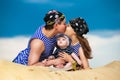 Happy family, mom, dad and little son in striped vests having fun in the sand outdoors against blue sky background. Summer Royalty Free Stock Photo