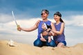 Happy family, mom, dad and little son in striped vests having fun in the sand outdoors against blue sky background. Summer Royalty Free Stock Photo