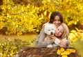 Happy family mom and daughter with little white dog hug and laugh sunny autumn day on the background of yellow leaves Royalty Free Stock Photo