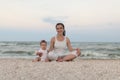 Happy family mother and child daughter doing yoga, meditate in lotus position on beach at sunset Royalty Free Stock Photo