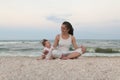 Happy family mother and child daughter doing yoga, meditate in lotus position on beach at sunset Royalty Free Stock Photo