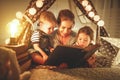 Happy family mother and children reading a book in tent at hom