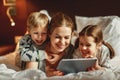 Happy family mother and children with tablet computer at home in bed in   evening Royalty Free Stock Photo