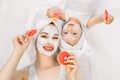 Happy family, mother and cute little daughter in white t-shirts and white towels on their heads lying on bed, doing Royalty Free Stock Photo