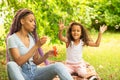 Happy family, mother and daughter play in nature, the child catches soap bubbles, an African woman and a girl in the park