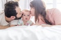 Happy family, mother, father and baby on the white bed giving side kiss Royalty Free Stock Photo