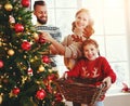 Happy family mother, father and child daughter decorate Christmas tree