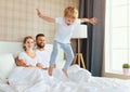 Happy family mother, father and child laughing, playing and jumping in bed