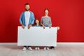 Happy family mother father and children daughter and son  near an   red wall with a white blank poster Royalty Free Stock Photo