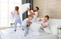 Happy family mother, father and children laughing, playing, fights pillows and jumping in bed at home