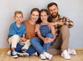 Happy family mother father and children sitting on floor against empty grey wall Royalty Free Stock Photo