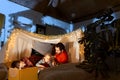 Happy family, mother, father and daughter lying inside self-made hut, tent in room in the evening. Cozy time with Royalty Free Stock Photo