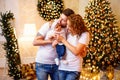 Happy family. Young parents hugging and kissing little baby girl while standing near Christmas tree Royalty Free Stock Photo